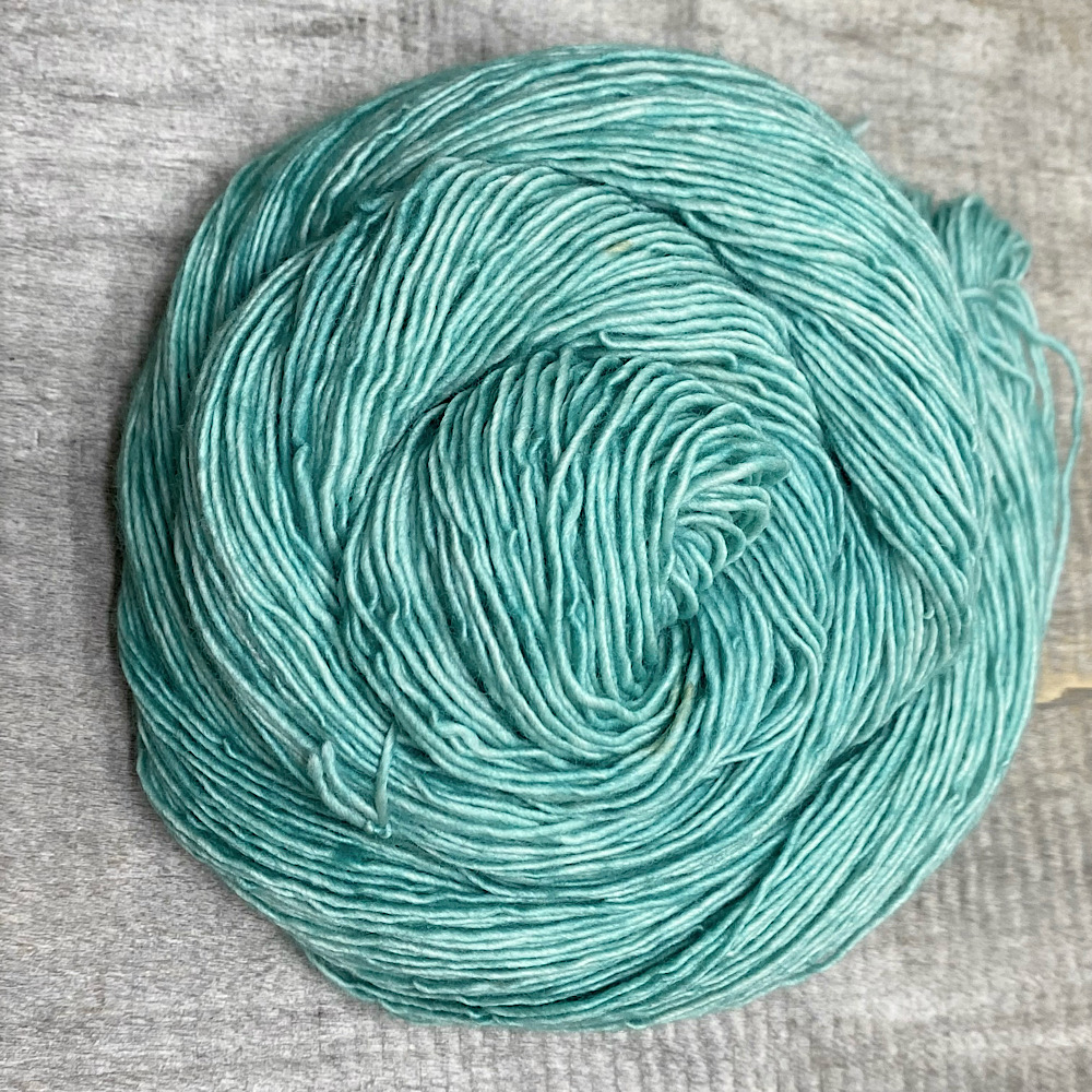 A swirl of single spun Merino wool in colour 'Celadon'. A semi-solid dye style in sea greens.