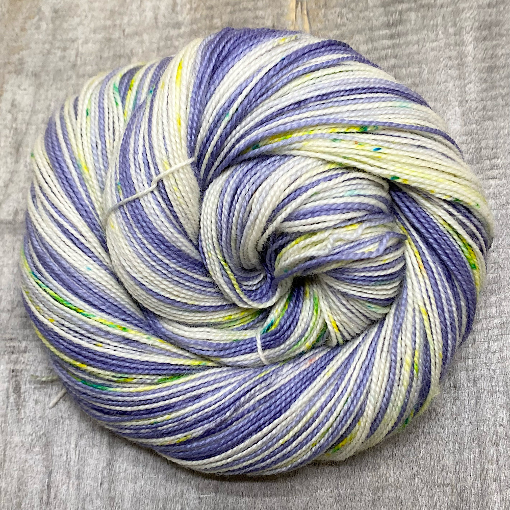 A swirled skein of hand dyed, pure BFL wool, spun with a twist, in colour 'Lullaby'. Hand painted sections in lavender tones, with yellows, violet and greens sprinkled over the remaining bare wool.