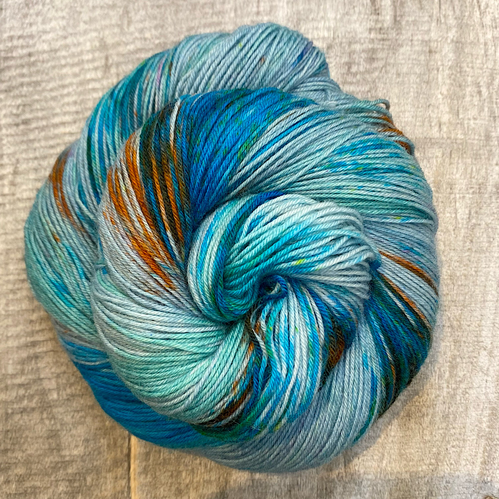 Hand dyed wool, 'Under the Sea', displayed as a swirl.. Colours are sea green tones and blue tones with rust coloured speckles.