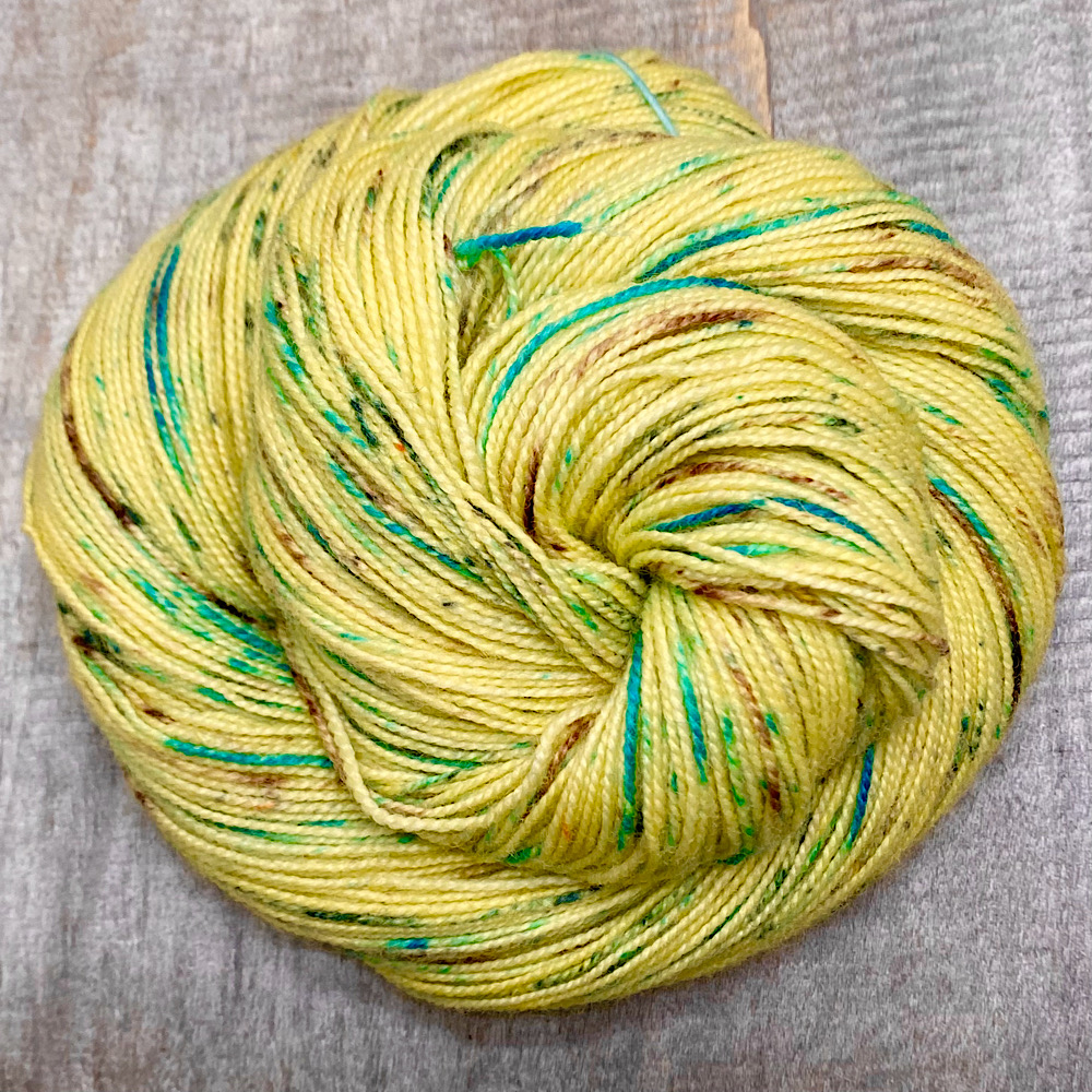 A swirled skein of hand dyed, pure BFL wool, spun with a twist, in colour 'Lullaby'. Dyed in a mid-yellow, then sprinkled with green and brown dye powders.